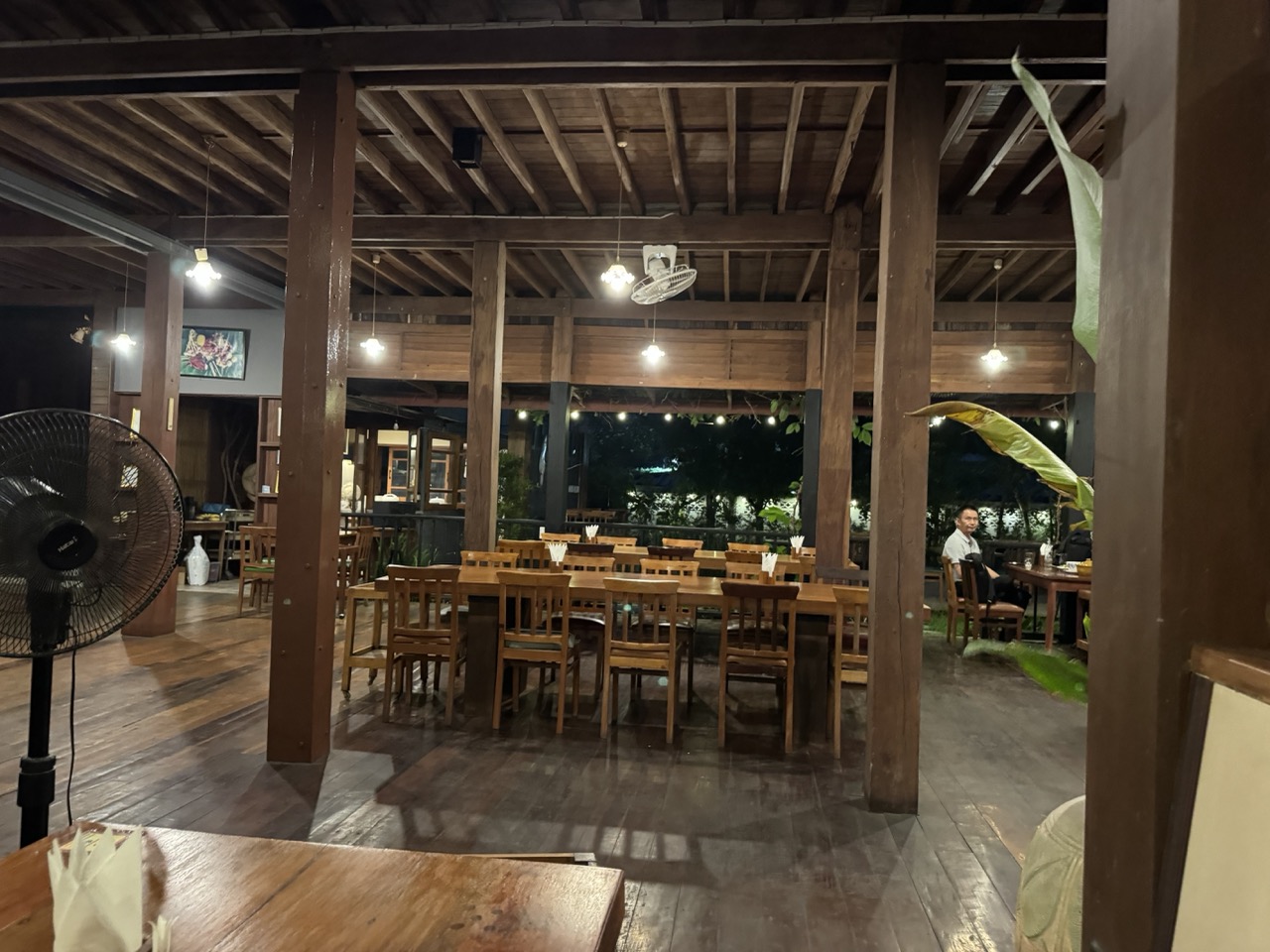 Open-air teak restaurant at night — the Riverhouse's own kitchen, on the river deck.
