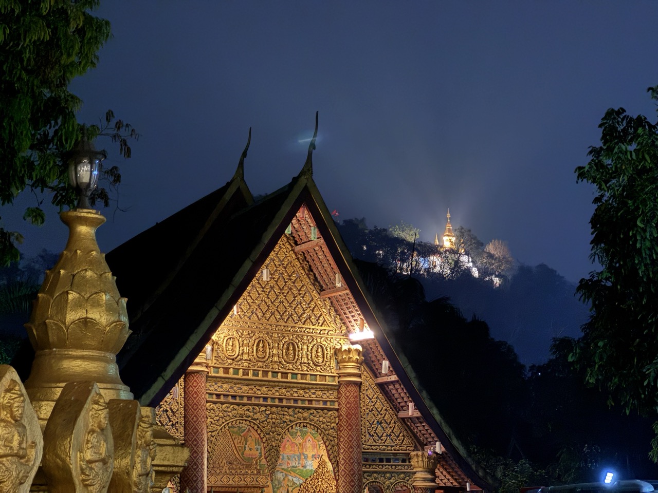 A gabled wat below Phou Si stupa, lit up at night.