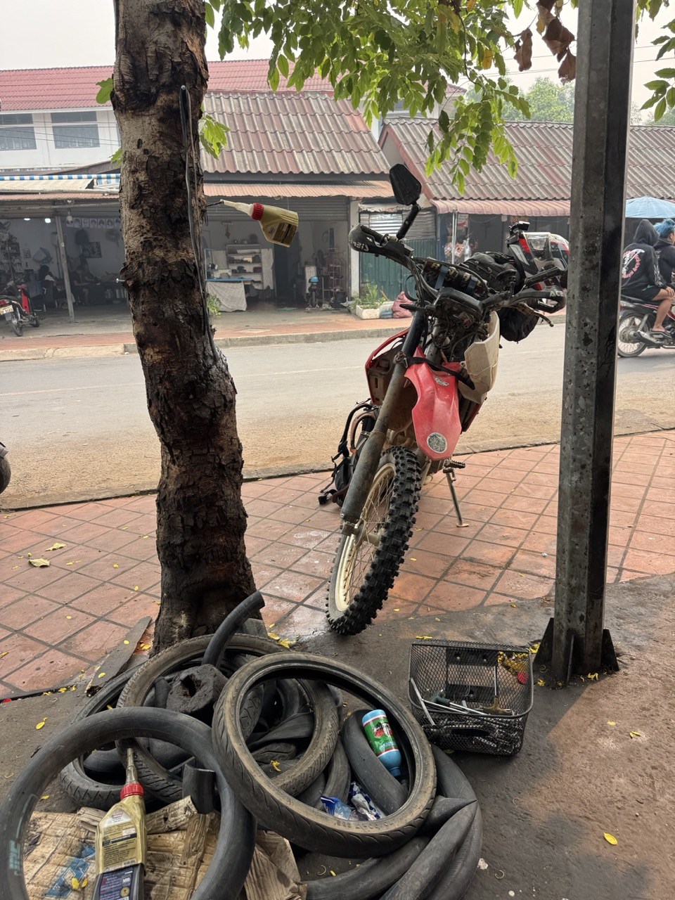 The CRF settled in at a Luang Prabang mechanic shop. Tire pile in the corner, dog asleep behind it.