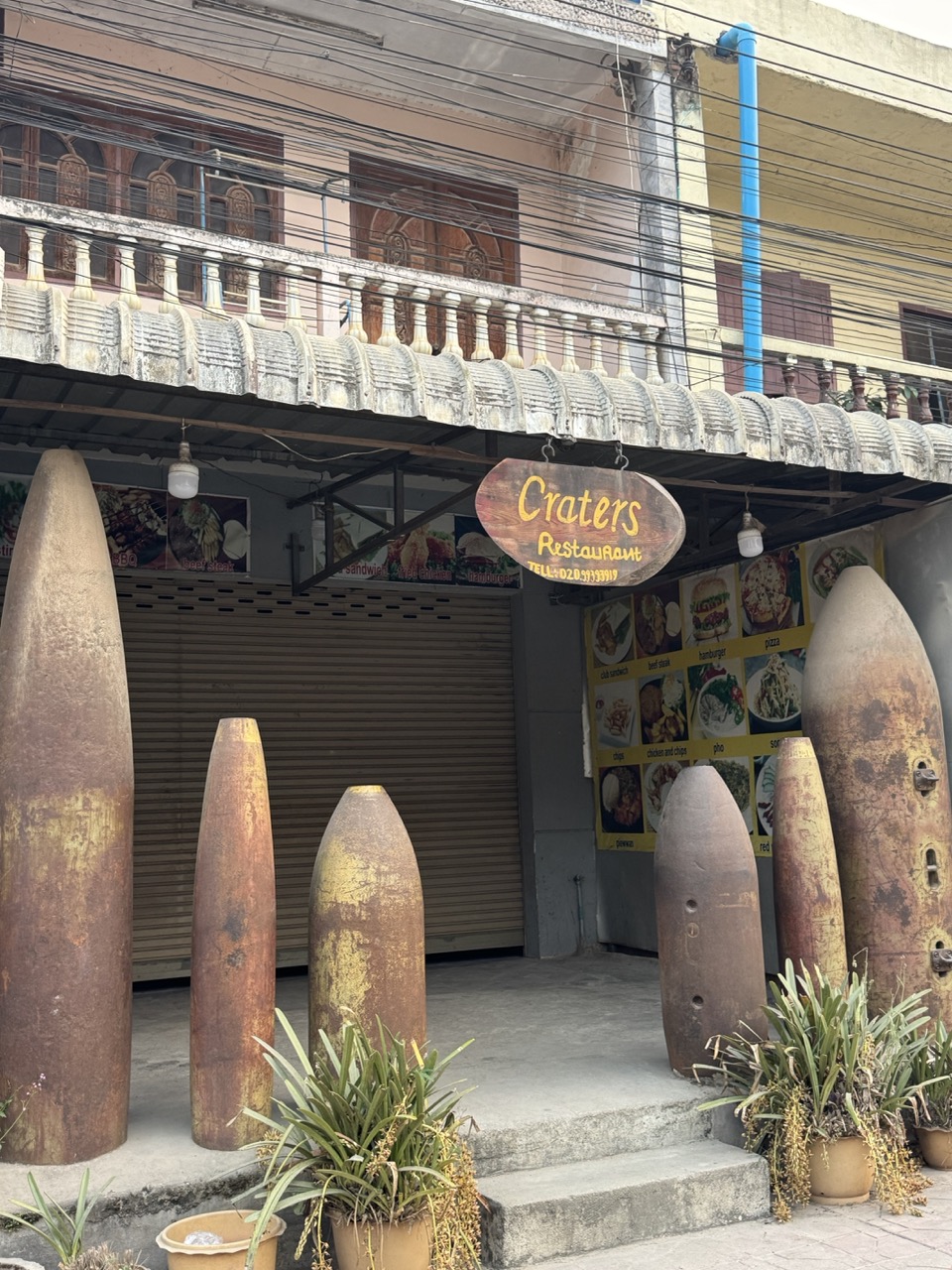 Craters Restaurant in Phonsavan — UXO bomb shells lined up outside as decor. Specifically themed around the Vietnam War / Secret War context that defines this region.