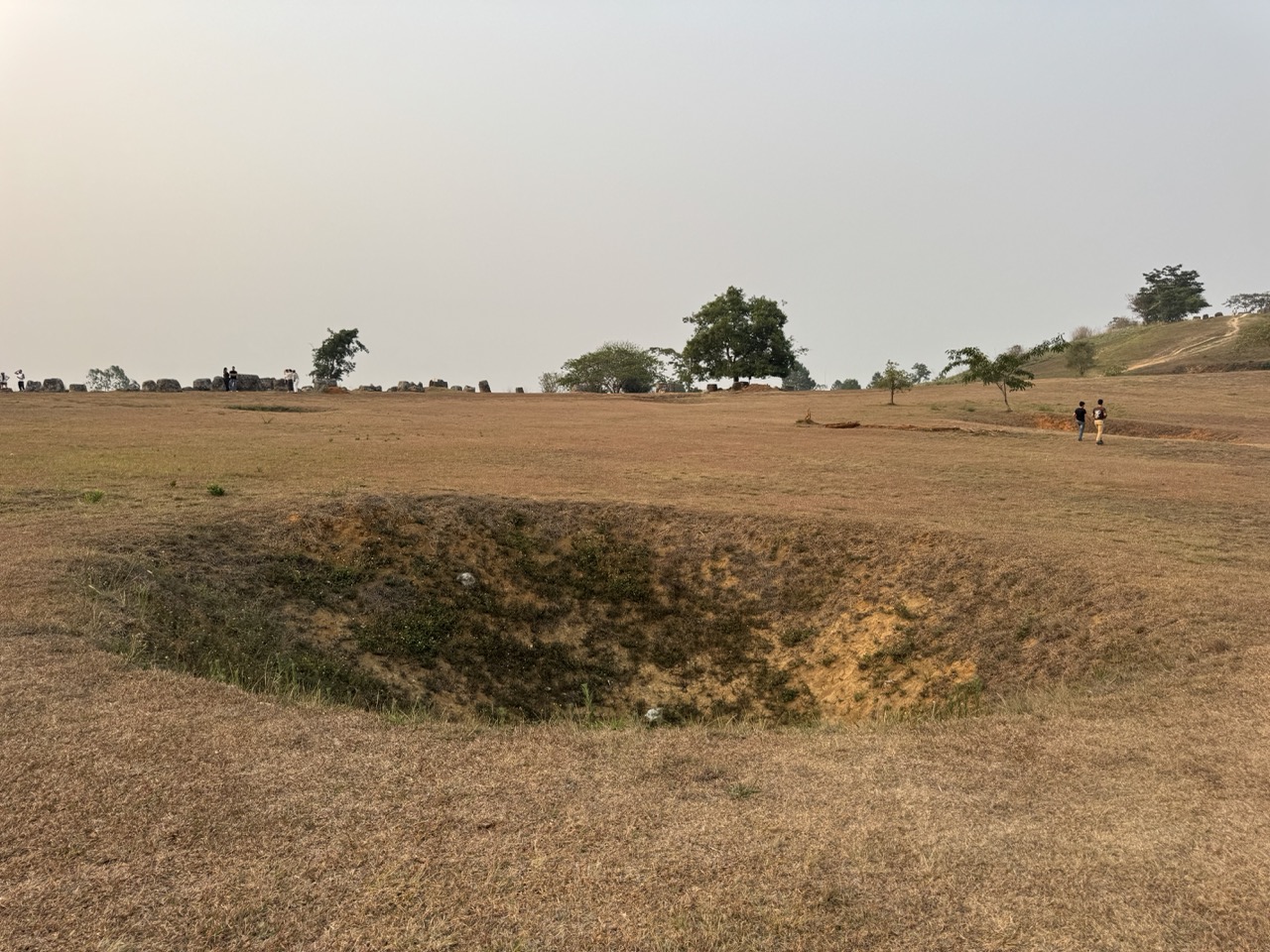 A Vietnam War bomb crater, mid-field. The Site 1 ground was repeatedly bombed during the Secret War — the craters are now part of the landscape.