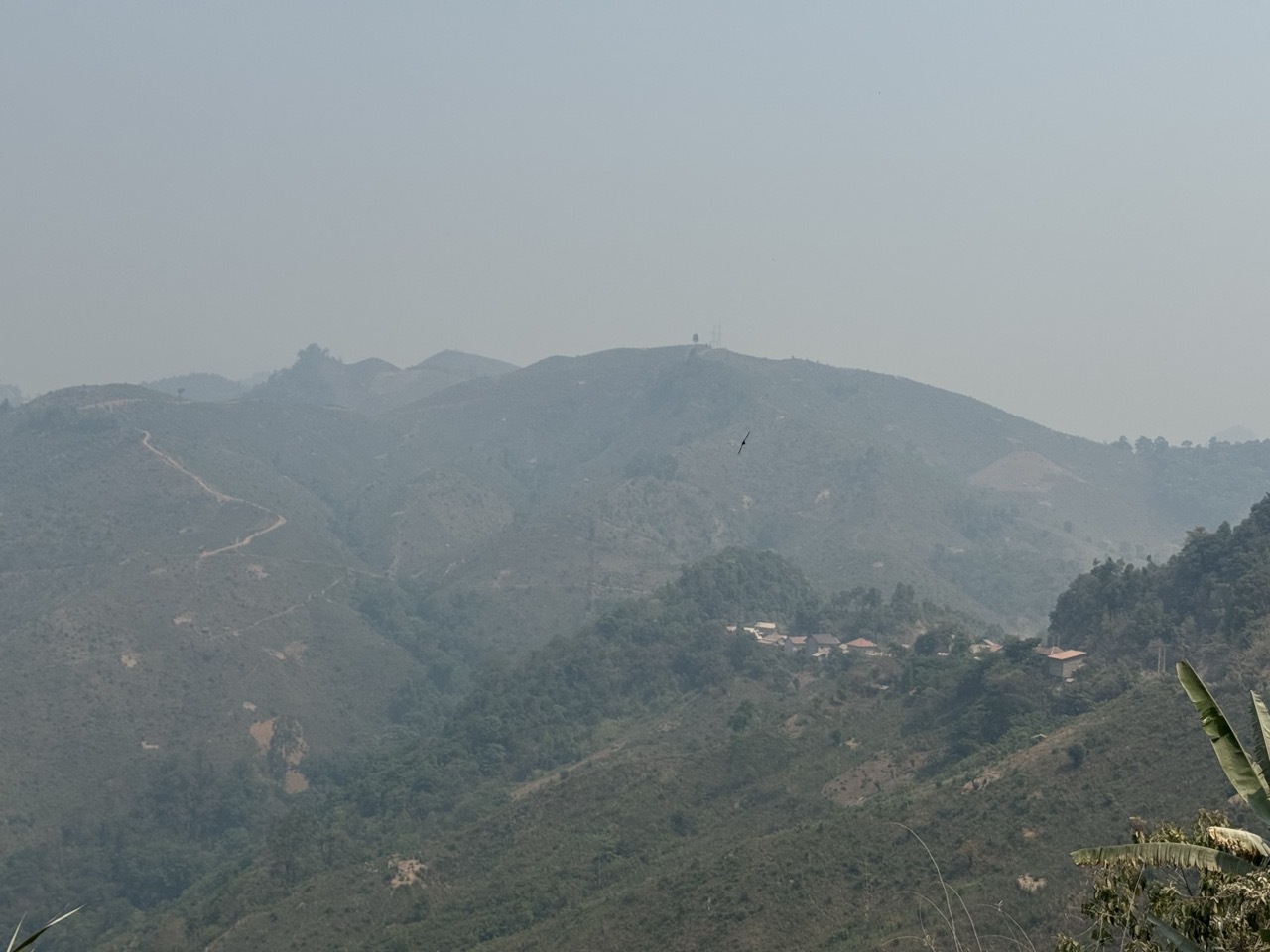 Hazy mountain pass with a distant tower-and-village in the next valley.