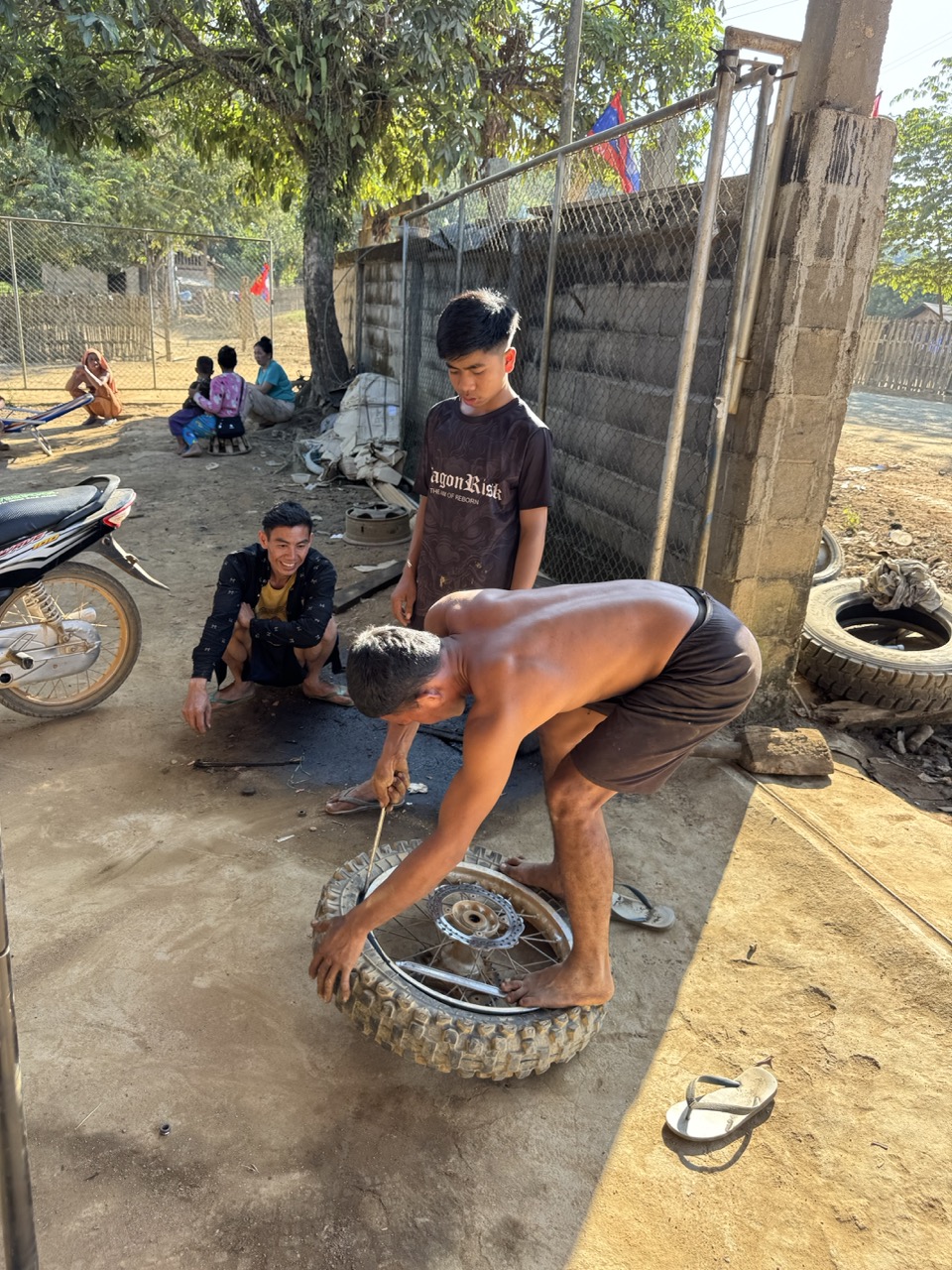 Tire shop stop somewhere near Muang Long — a local mechanic and his helper fixing one of the CRF wheels in the dust outside the workshop.
