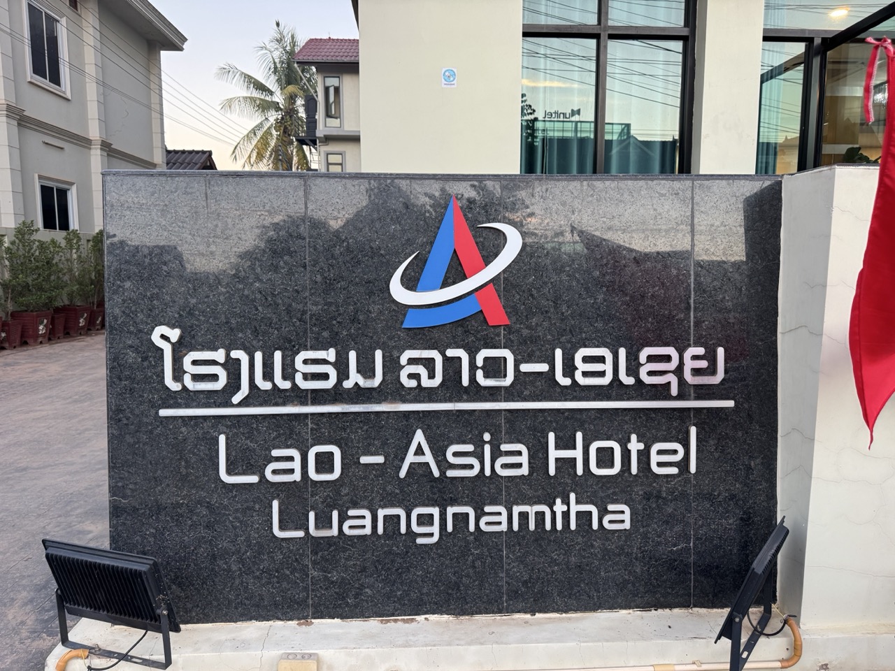 Lao-Asia Hotel arrival — clean stone sign in Lao and English, friendly staff, good parking for the bikes.