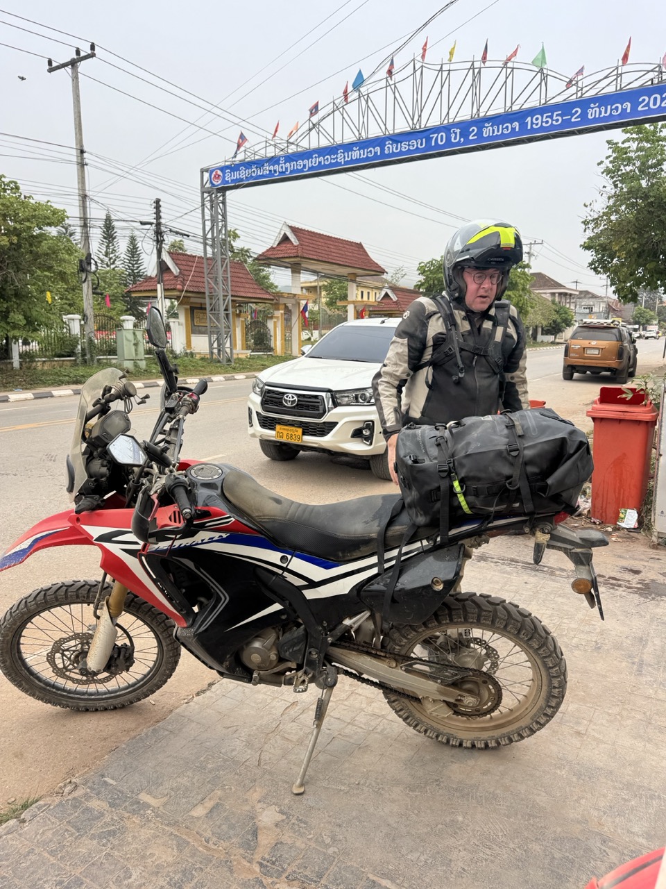 Rolling out of Luang Namtha past a 70-year national anniversary banner — 1955–2025.