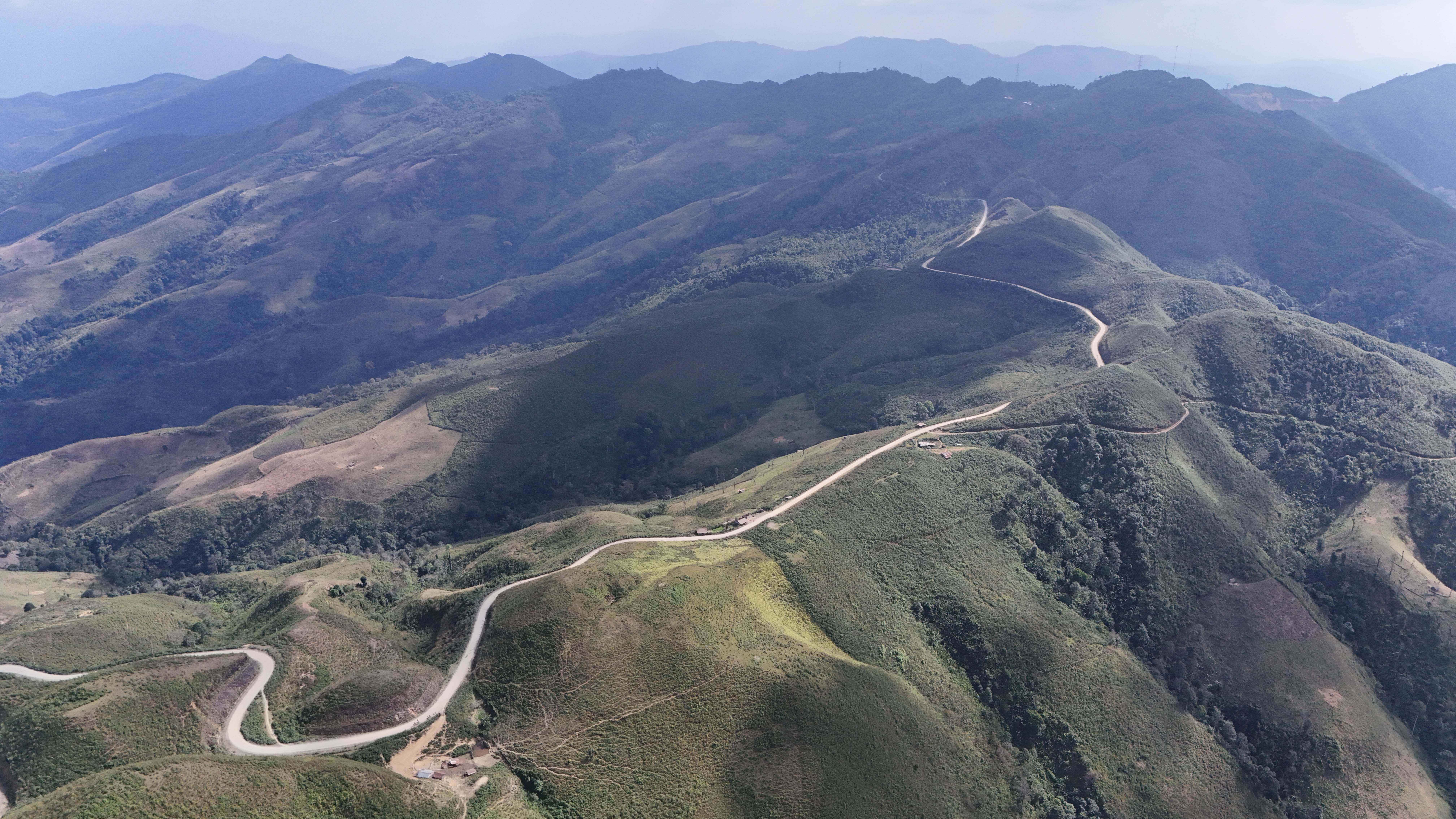 Drone view of the pass — a white ribbon of road switchbacking across the green ridges south of Phongsali.