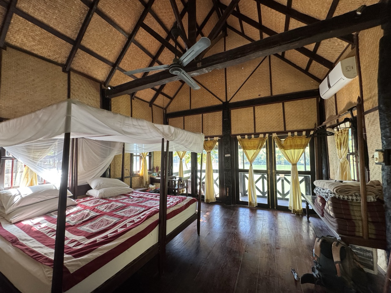 Inside a Nong Kiau Riverside bungalow — bamboo walls, A-frame beams, mosquito net, river-facing balcony.