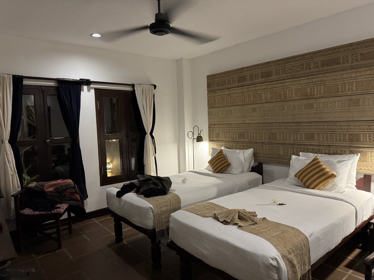 Victoria Xiengthong Palace, room view — twin beds, tribal-textile headboard panels, dark wood and gold accents.
