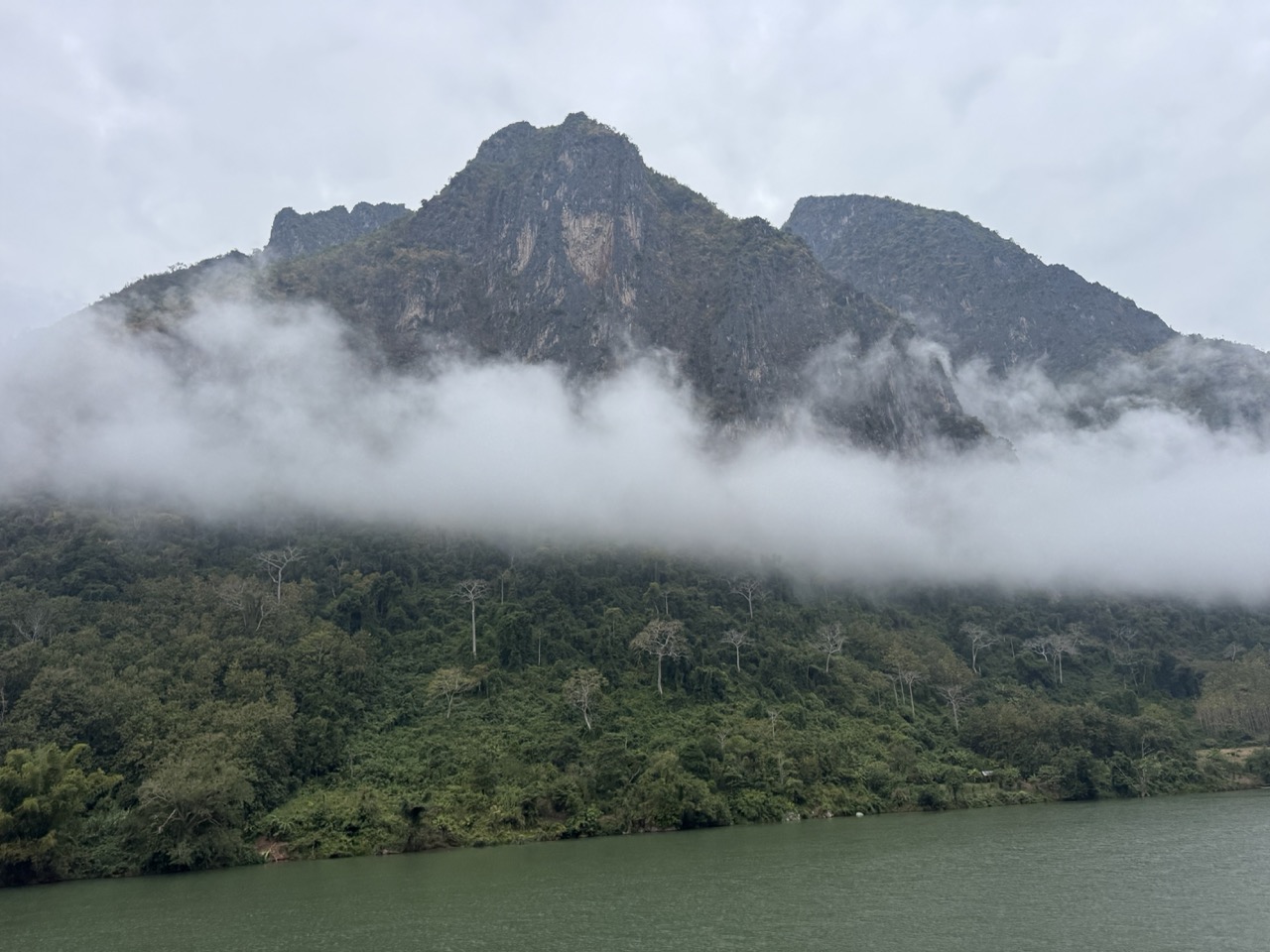 Morning departure view from the Nong Khiaw bridge — karst peak still wrapped in fog over the Nam Ou.