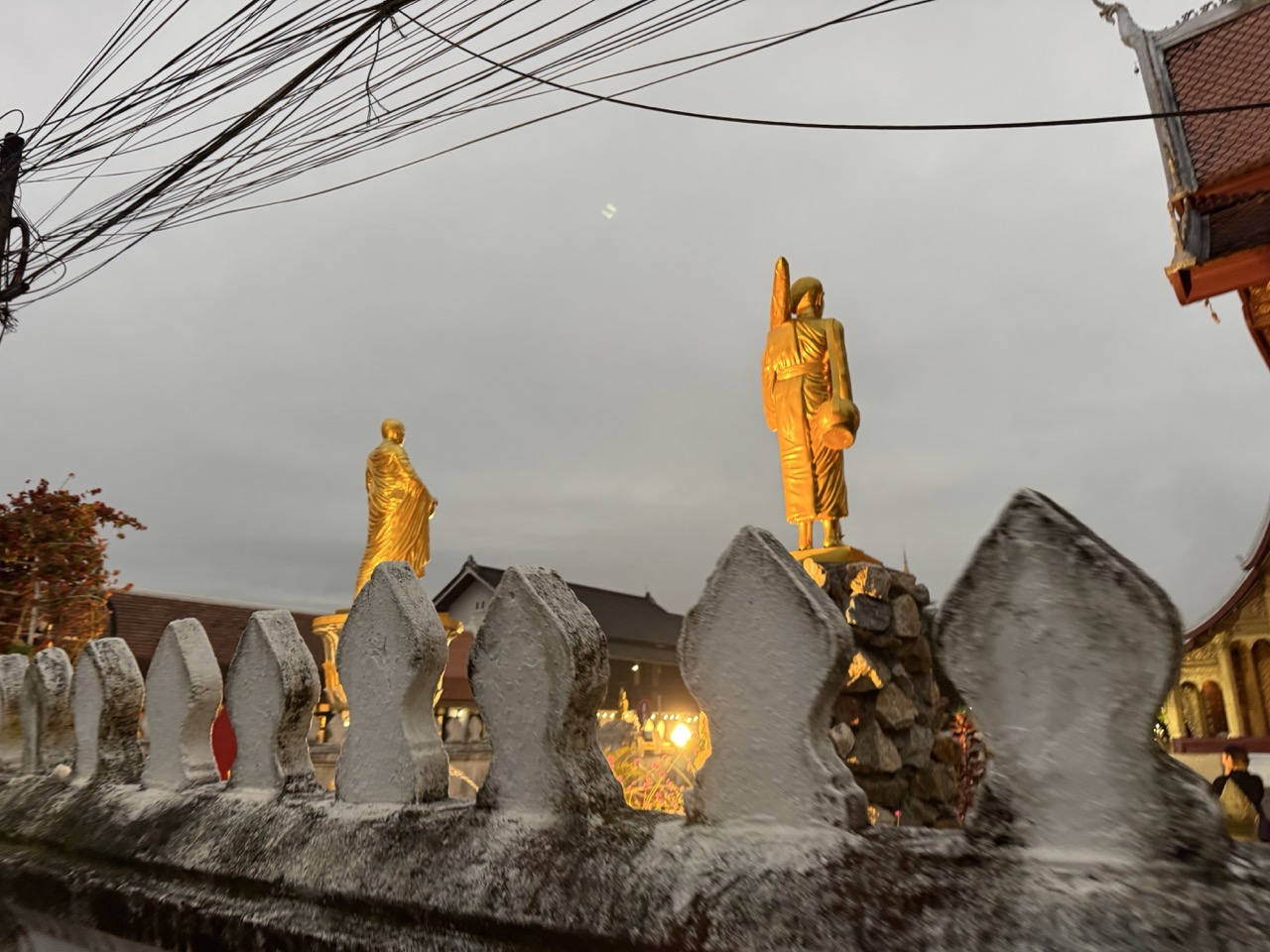 Wat in central Luang Prabang in evening light — gold-leaf monk statues against a stone wall.